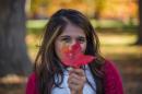 A UNH student holding a red leaf from a maple tree, with golden hues of foliage in the background